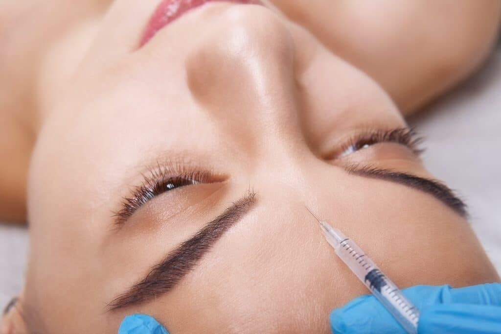 closeup portrait of young caucasian woman getting cosmetic injection of botox in forehead people