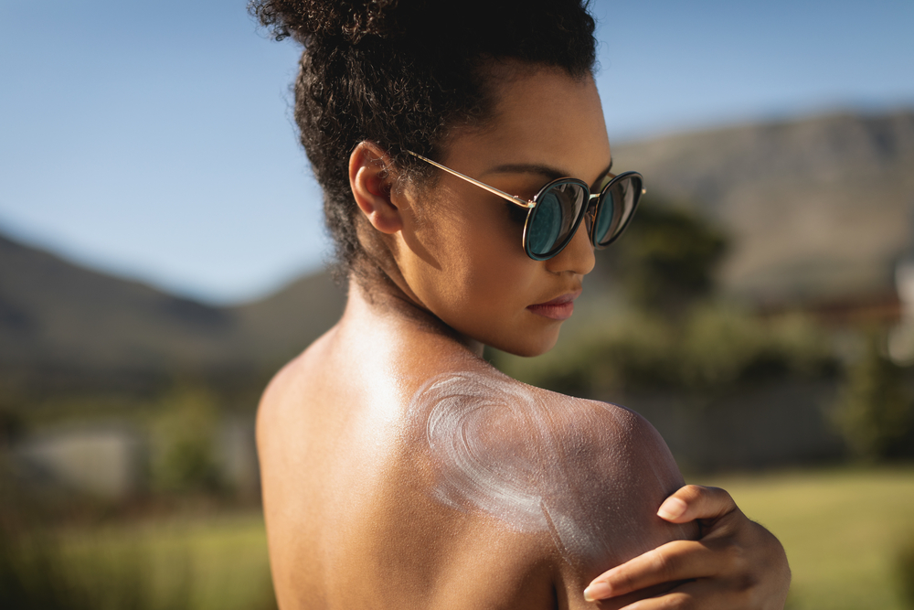Side view of young mixed race woman applying sunscreen on shoulders in backyard of home on a sunny day