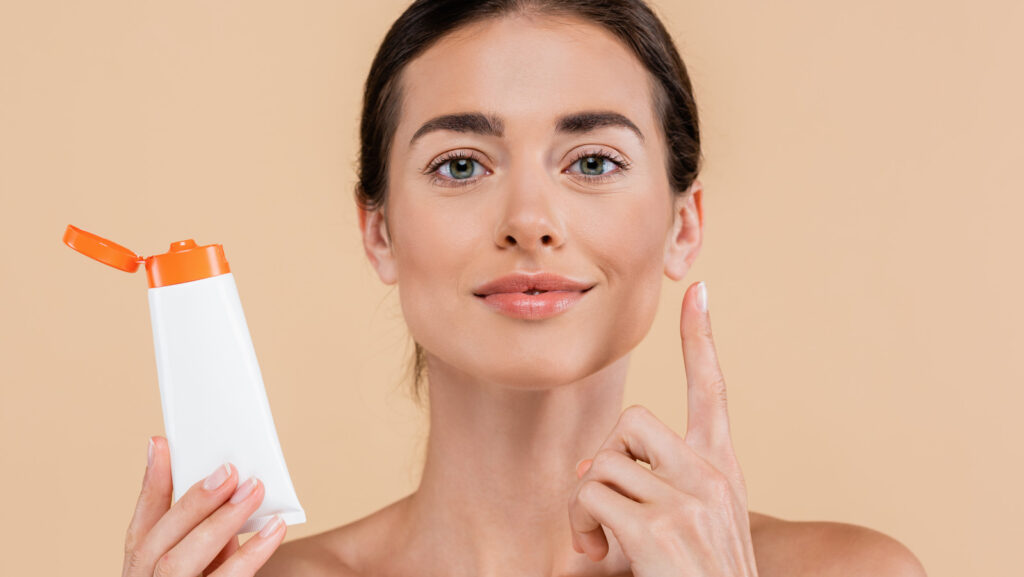 Brunette,Woman,Holding,Sunscreen,And,Pointing,Up,With,Finger,Isolated